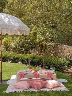 an outdoor table set up with pink pillows and white umbrellas, in the middle of a garden