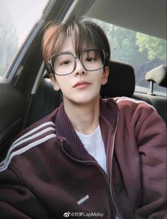 a young man wearing glasses sitting in a car