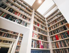 a room filled with lots of books next to a ceiling mounted skylight on top of a white wall