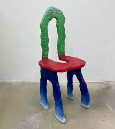 a chair made out of paper mache and colored paint sitting on the floor in front of a white wall