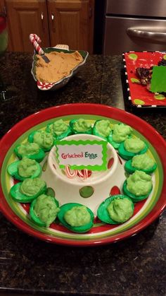 a plate with green frosted cookies on top of it next to a red bowl filled with cupcakes