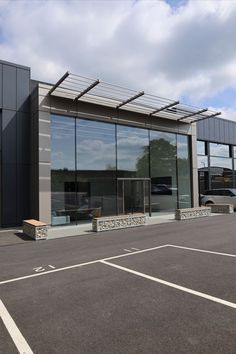 an empty parking lot in front of a building with glass doors and benches on the outside