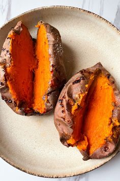 two baked sweet potatoes on a plate with one cut in half to show the inside