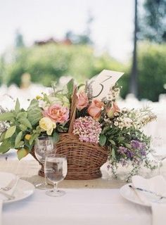 the table is set with white linens and pink flowers in a wicker basket