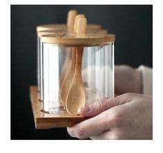 a person holding a glass container with wooden spoons in it