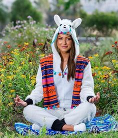 a woman sitting in the middle of a field with her eyes closed and wearing an animal hat