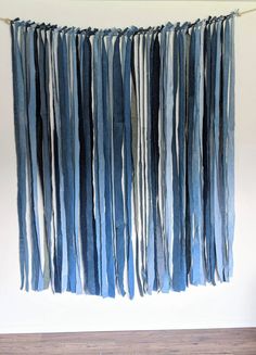 a blue and white wall hanging with strips of yarn on the bottom, in front of a wooden floor