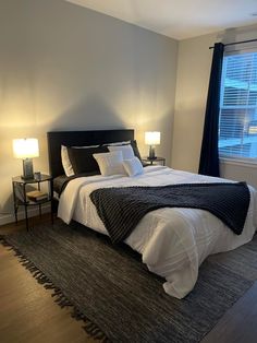 a bedroom with a large bed and two lamps on either side of the bed, in front of a window