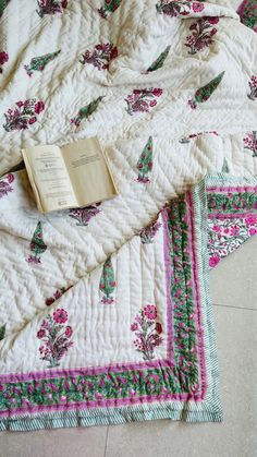 an open book is laying on top of a quilted bed spread with pink and green flowers