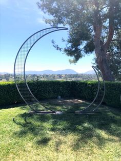 two metal sculptures sitting in the middle of a grass covered field next to a tree