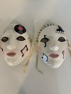 two white masks with black and red designs on them, one has a yellow ribbon