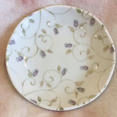 a white plate with purple flowers on it sitting on a pink tableclothed surface