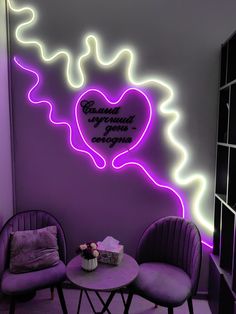 two purple chairs sitting in front of a table with a heart on it's wall