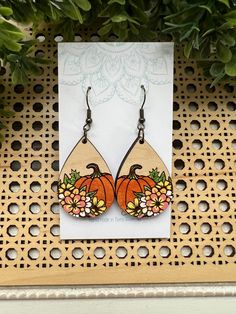 a pair of wooden earrings with flowers and pumpkins painted on them sitting in front of a plant