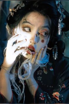 a woman with makeup on her face and hands in front of her face, wearing an elaborate headdress