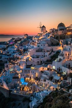 the sun is setting over some white buildings and windmills in oia, greece