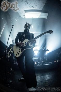 a man with a guitar in front of some microphones and stage lights, wearing a horned headdress