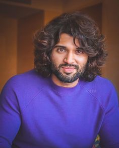 a man with long hair wearing a purple sweater