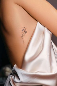 the back of a woman's shoulder with a small flower tattoo on her left side