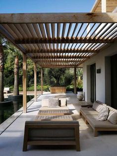 an outdoor living area with couches and tables on the side of the house, covered in wood slats