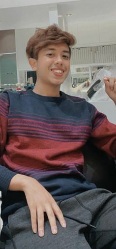 a young man sitting on top of a couch holding a remote control in his hand