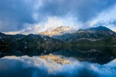 the mountains are covered in snow and clouds as they sit on top of a lake