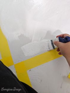 someone using a brush to paint a wall with white and yellow stripes on it,