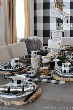 a dining room table set with black and white checkered placemats, candles, plates and cups