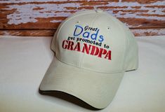 "Don't forget about Grandpa on Father's Day, first time Grandpa or his birthday! This hat is a great reminder of how important he really is! \"Great Dads get promoted to Grandpa\" is embroidered on a white cap. If you love this design but not the hat color, let me know. I have several hat styles and thread colors to choose from, just CONVO me and I'll be happy to help! It is also very easy to change the wording Grandpa to Papa, PopPop, Pops, etc. SOLID COLOR HATS -100% peach-washed cotton -Struc Father's Day Gift Baseball Cap With Curved Brim, Father's Day Gift Snapback Hat With Curved Brim, Letter Print Hat For Father's Day Gift, Father's Day Gift Hats With Letter Print, Curved Brim Baseball Cap For Father's Day, Personalized Hats For Father's Day, Father's Day Dad Hat Gift, Flat Bill Hats For Father's Day Gift, Father's Day Gift Flat Bill Hat