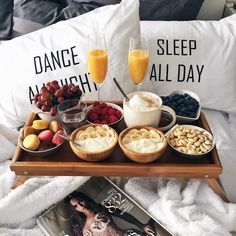 a tray filled with food on top of a bed next to two glasses of orange juice