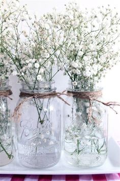 three mason jars filled with baby's breath flowers on a checkered table cloth