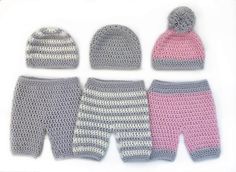 crocheted baby clothes and hats are displayed on a white surface, including one pink hat