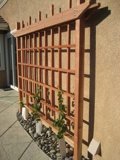 a wooden trellis sitting on top of a sidewalk next to a wall with potted plants