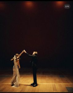 a man and woman dance on a wooden floor in an empty room with spotlights