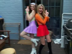 two young women dressed in short skirts and knee high boots posing for the camera with their hands up