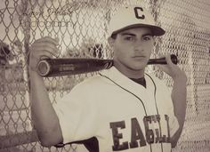 a young man holding a baseball bat next to a fence