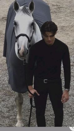 a man standing next to a horse with a blanket on it's head and holding the reins