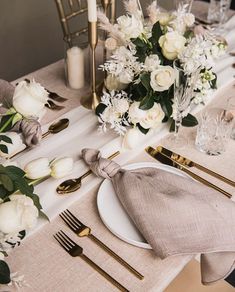 the table is set with white flowers and gold place settings