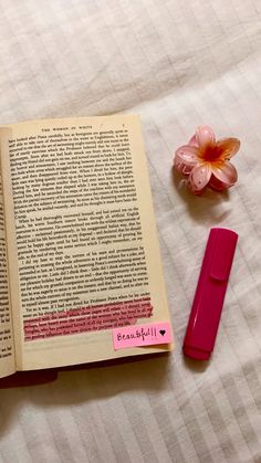 an open book next to a pink pen and flower