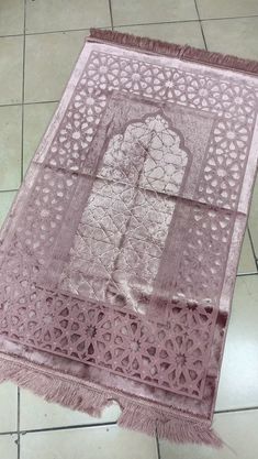 a pink rug with an intricate design on the top and bottom, sitting on a tile floor