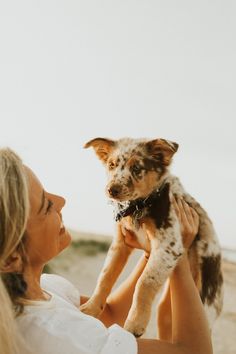 a woman holding a small dog in her arms on the beach while looking at the sky