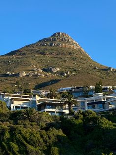 a mountain with houses on the top and trees around it, in front of a clear blue sky