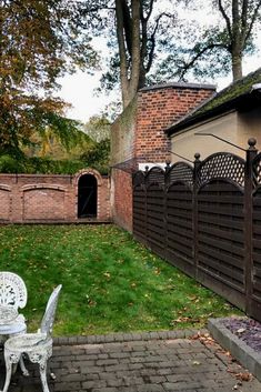 a white chair sitting on top of a brick patio next to a wooden fence and green grass