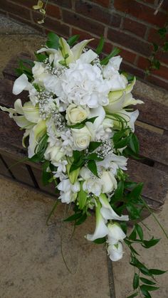 a bouquet of white flowers sitting on top of a wooden bench next to a brick wall