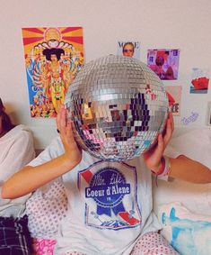 a person sitting on a bed with a disco ball in their hand and some posters behind them