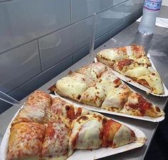 three slices of pizza sitting on top of white paper plates in front of a metal counter