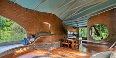 a person sitting on a couch in a room with brick walls and round windows that look out onto the jungle