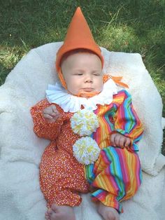 a baby in a clown outfit laying on a blanket with a hat and flowers around its neck