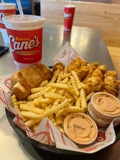 a basket filled with fried chicken, french fries and coleslaw next to two cups of soda