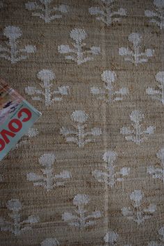 a magazine laying on top of a bed next to a wallpaper covered in white flowers